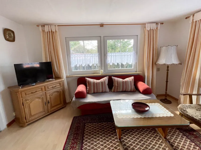 Gemütliches Wohnzimmer mit Couch, Flat-TV und großen Fenstern zum Garten
